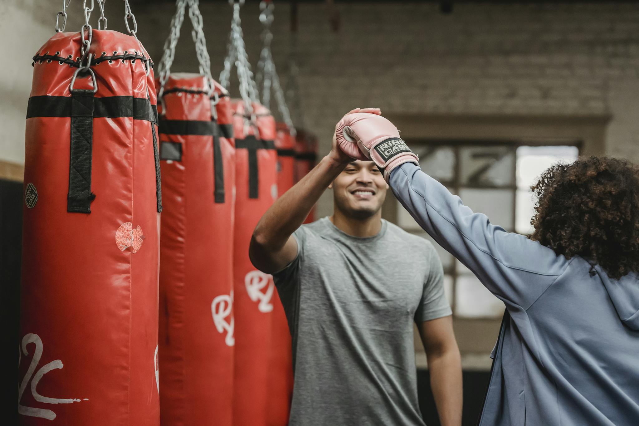 Positive ethnic male coach having high five with female after boxing training in gym with punching bags
