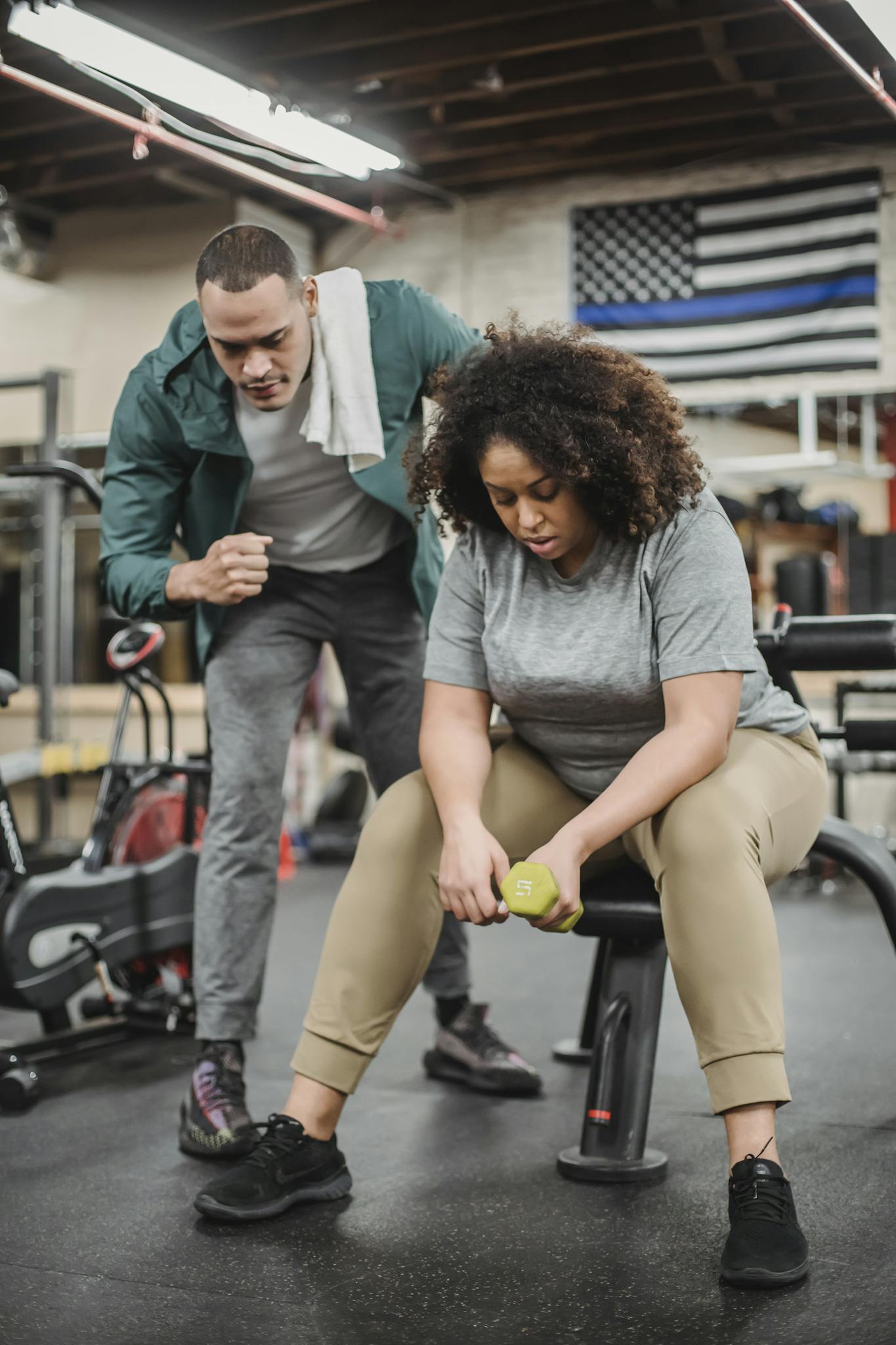 Trainer helping plump woman exercising with dumbbell